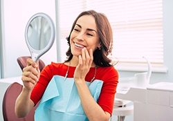 Woman at dentist’s office smiling into hand mirror 