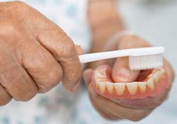 Closeup of hands scrubbing dentures with white toothbrush