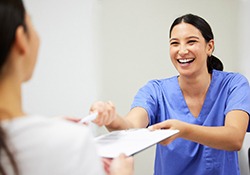 Dental assistant smiling while handing patient forms