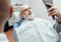An older man admiring his dentures in a hand mirror
