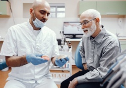 A dentist showing an older man how dentures will fit into his mouth using a special mold
