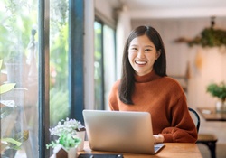 A young woman seated behind a laptop and wearing a sweater, smiling after undergoing dental tooth bonding in Harrisonburg