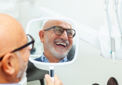 Senior man admiring his new smile in dental clinic mirror