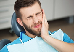 Man in dental chair holding cheek