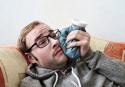 A man lying on the couch with an ice pack on his cheek
