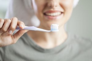 smiling woman in background holding toothbrush with toothpaste in foreground