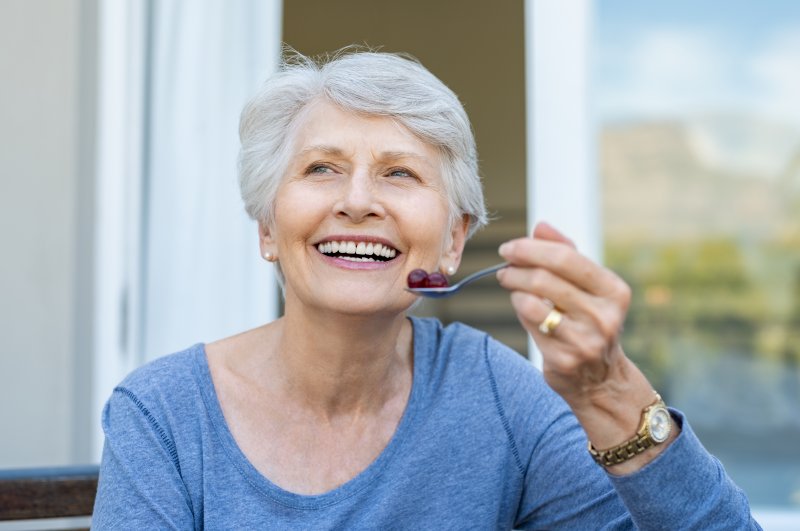 an older woman wearing a blue blouse and eating grapes outside and smiling