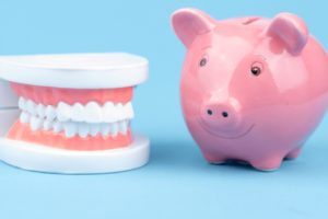 Smiling piggy bank next to dental model, illustrating affordable dentures