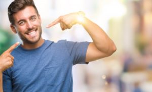 man with a dental crown pointing to his smile 