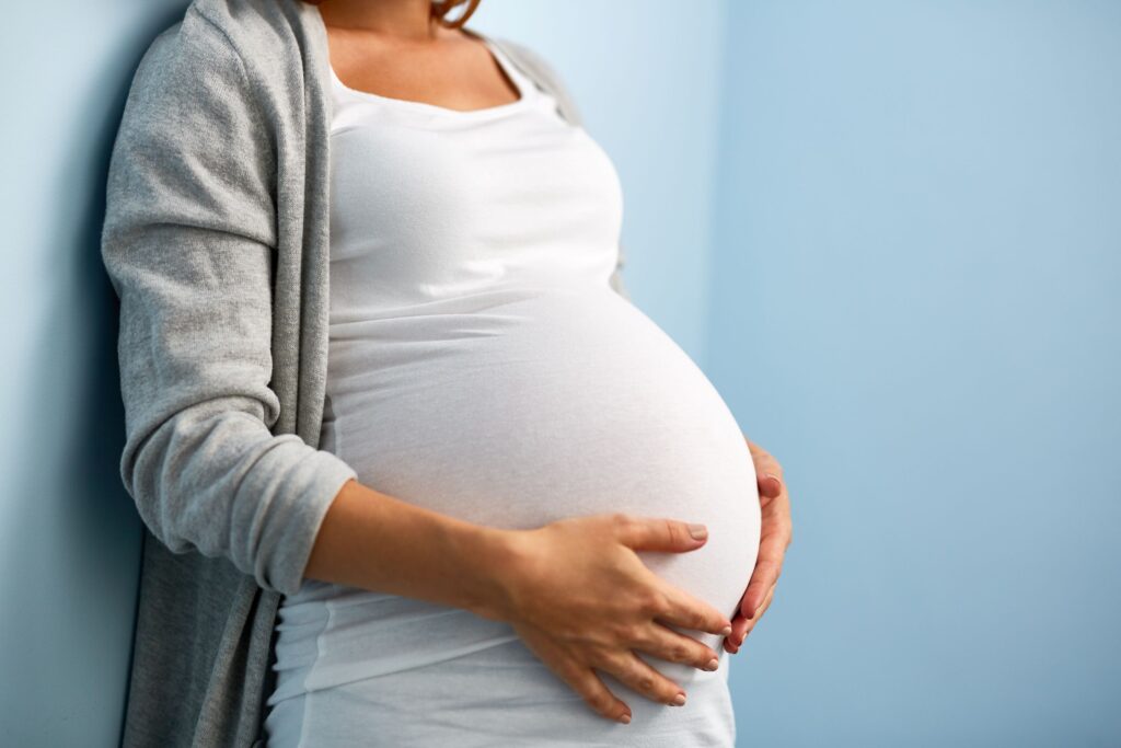 Abdomen-only view of woman placing hands on her pregnant belly